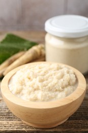 Photo of Tasty horseradish sauce and roots on wooden table, closeup