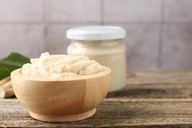 Photo of Tasty horseradish sauce and roots on wooden table, closeup. Space for text