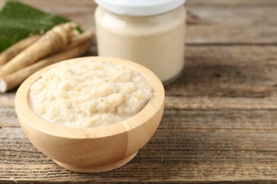 Photo of Tasty horseradish sauce and roots on wooden table, closeup. Space for text