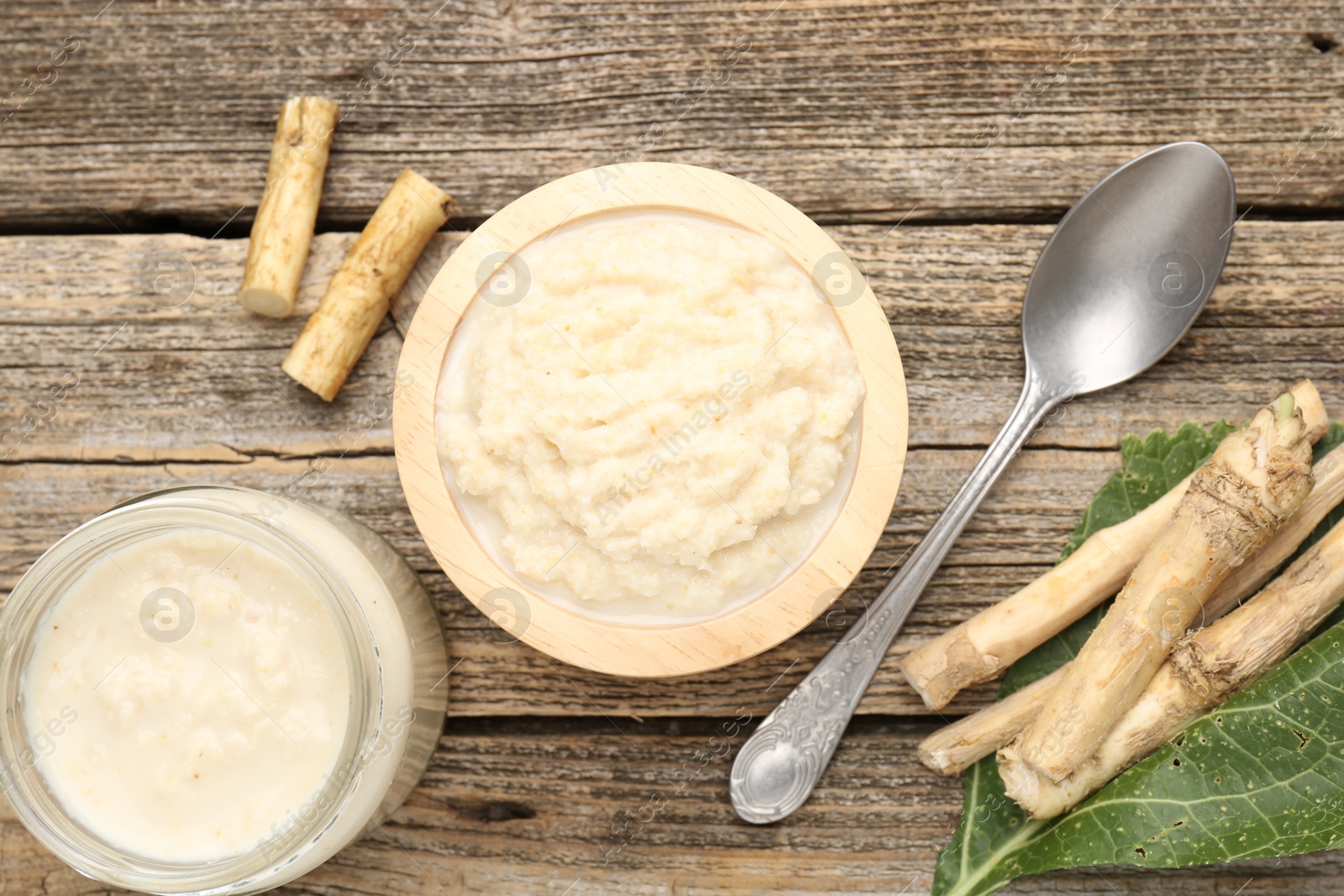 Photo of Tasty horseradish sauce, spoon and roots on wooden table, flat lay