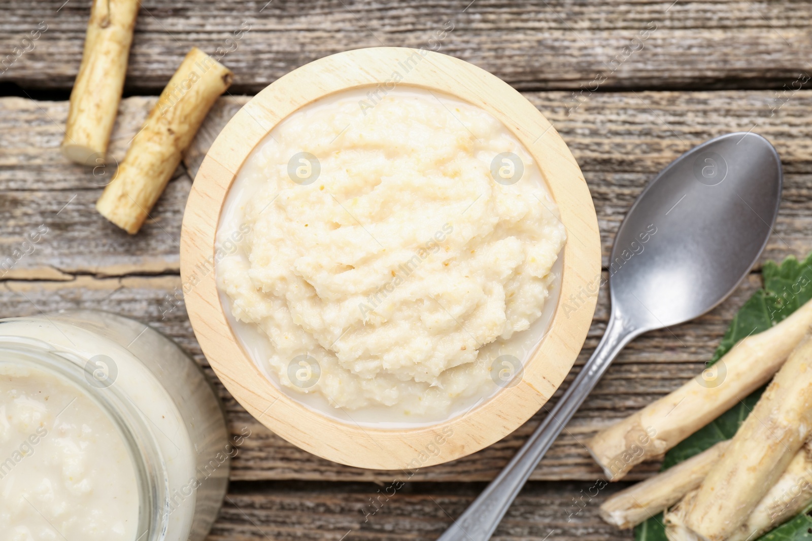 Photo of Tasty horseradish sauce, spoon and roots on wooden table, flat lay