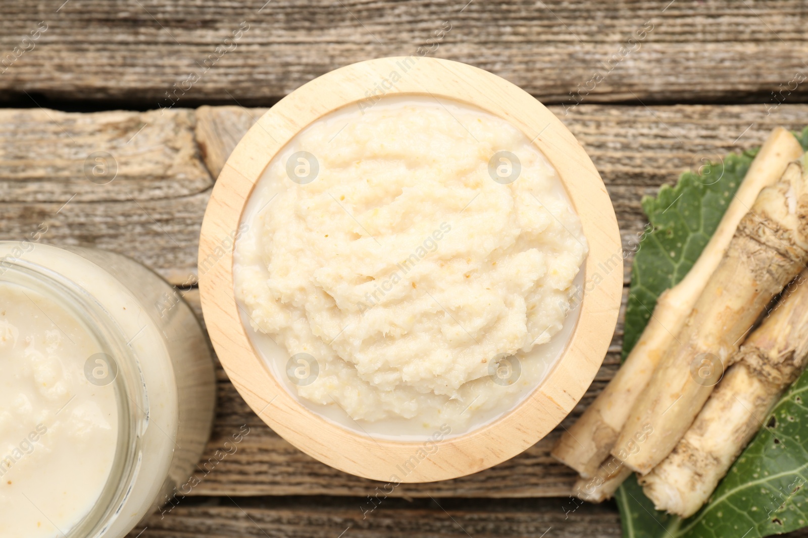 Photo of Tasty horseradish sauce and roots on wooden table, flat lay