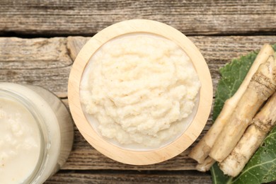 Photo of Tasty horseradish sauce and roots on wooden table, flat lay