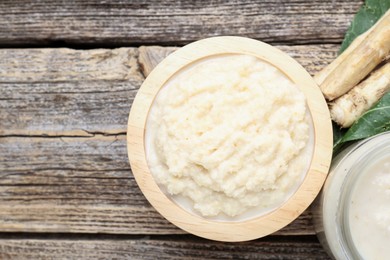 Photo of Tasty horseradish sauce and roots on wooden table, flat lay. Space for text