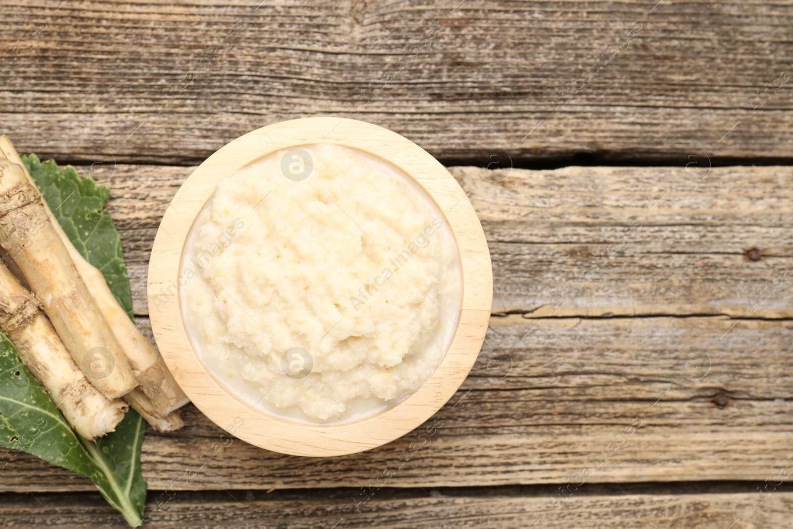 Photo of Tasty horseradish sauce and roots on wooden table, flat lay. Space for text