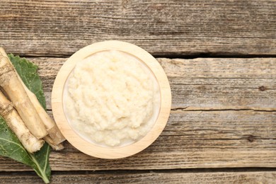 Photo of Tasty horseradish sauce and roots on wooden table, flat lay. Space for text