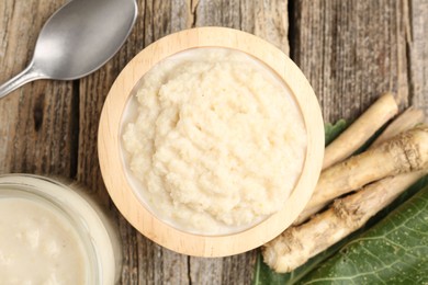 Photo of Tasty horseradish sauce, spoon and roots on wooden table, flat lay