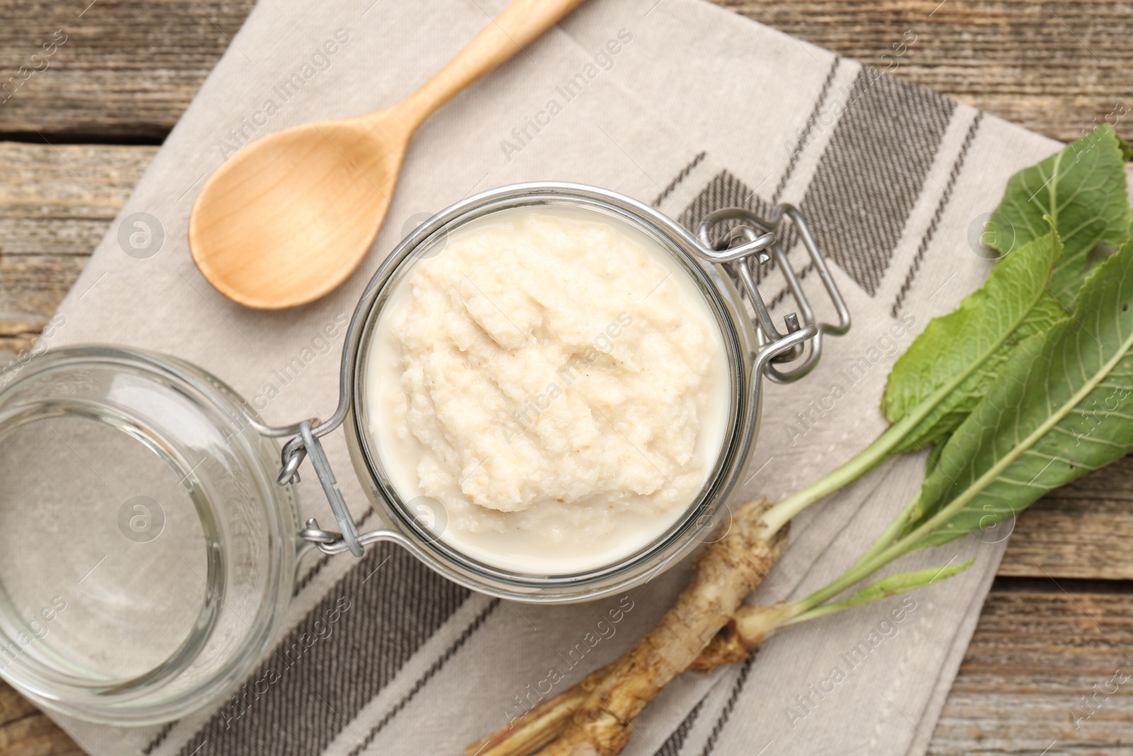 Photo of Tasty horseradish sauce, spoon and roots on wooden table, flat lay