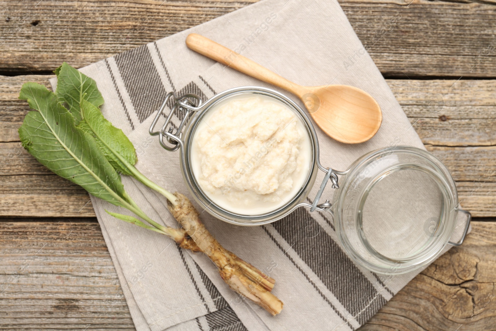 Photo of Tasty horseradish sauce, spoon and roots on wooden table, flat lay