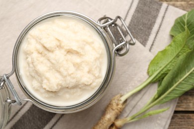 Photo of Tasty horseradish sauce and roots on wooden table, flat lay