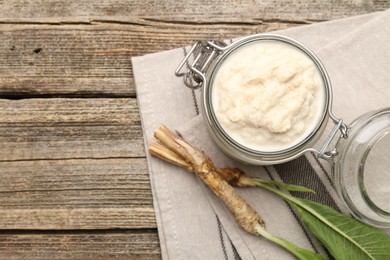 Photo of Tasty horseradish sauce and roots on wooden table, flat lay. Space for text