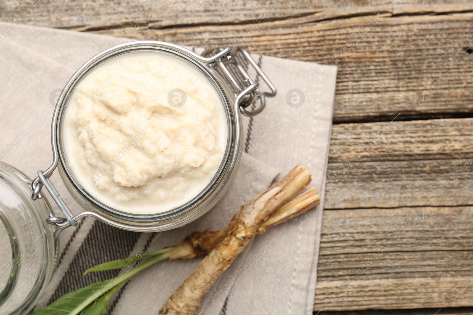 Photo of Tasty horseradish sauce and roots on wooden table, flat lay. Space for text