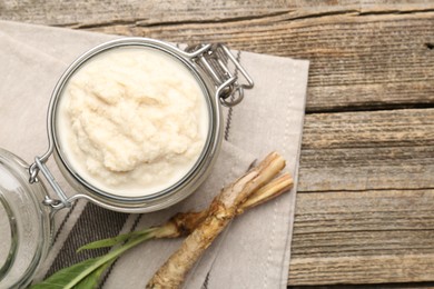 Photo of Tasty horseradish sauce and roots on wooden table, flat lay. Space for text