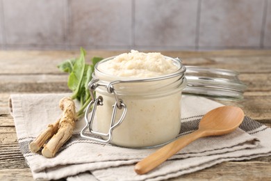 Photo of Tasty horseradish sauce, spoon and roots on wooden table, closeup
