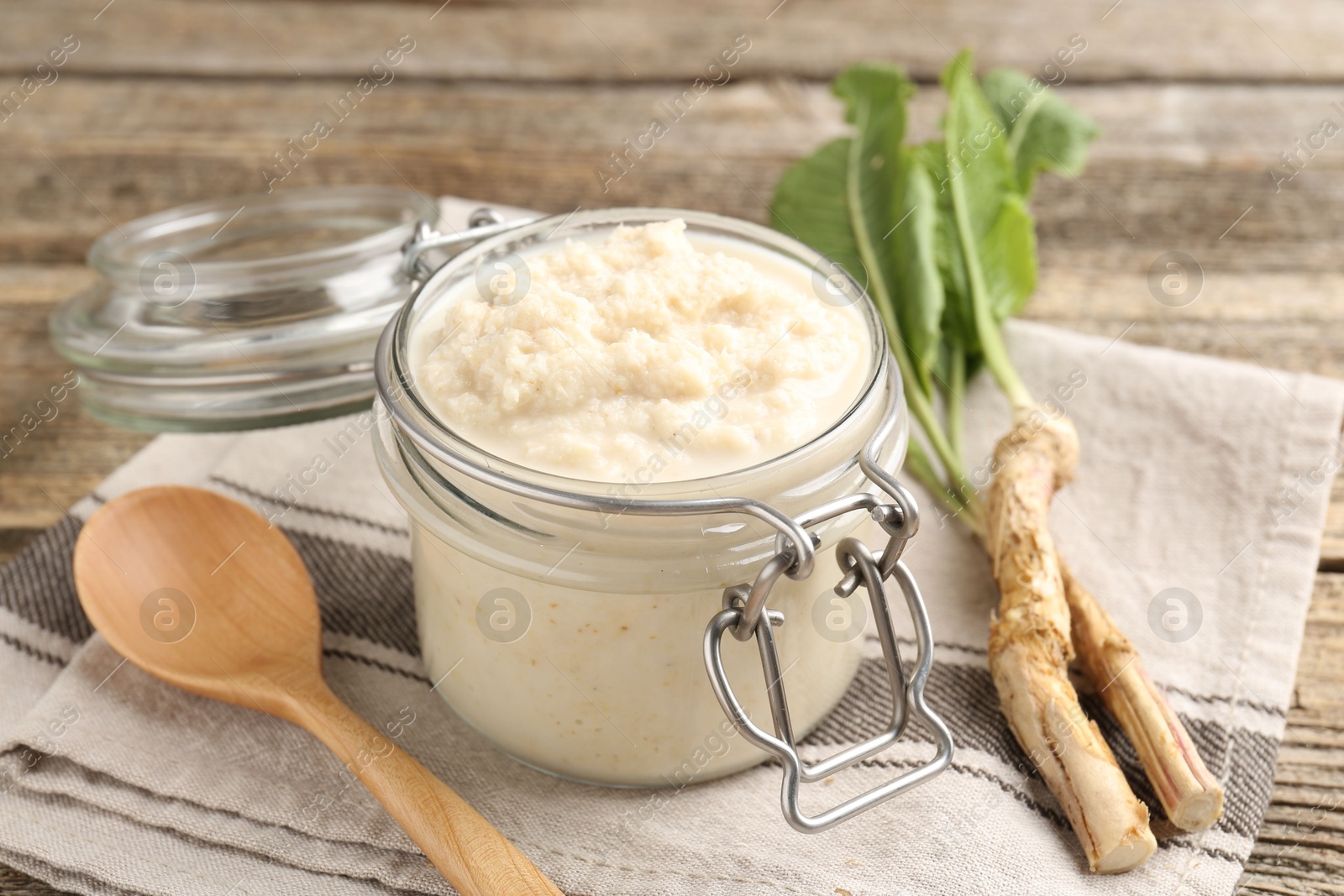Photo of Tasty horseradish sauce, spoon and roots on wooden table, closeup