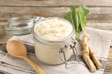 Photo of Tasty horseradish sauce, spoon and roots on wooden table, closeup