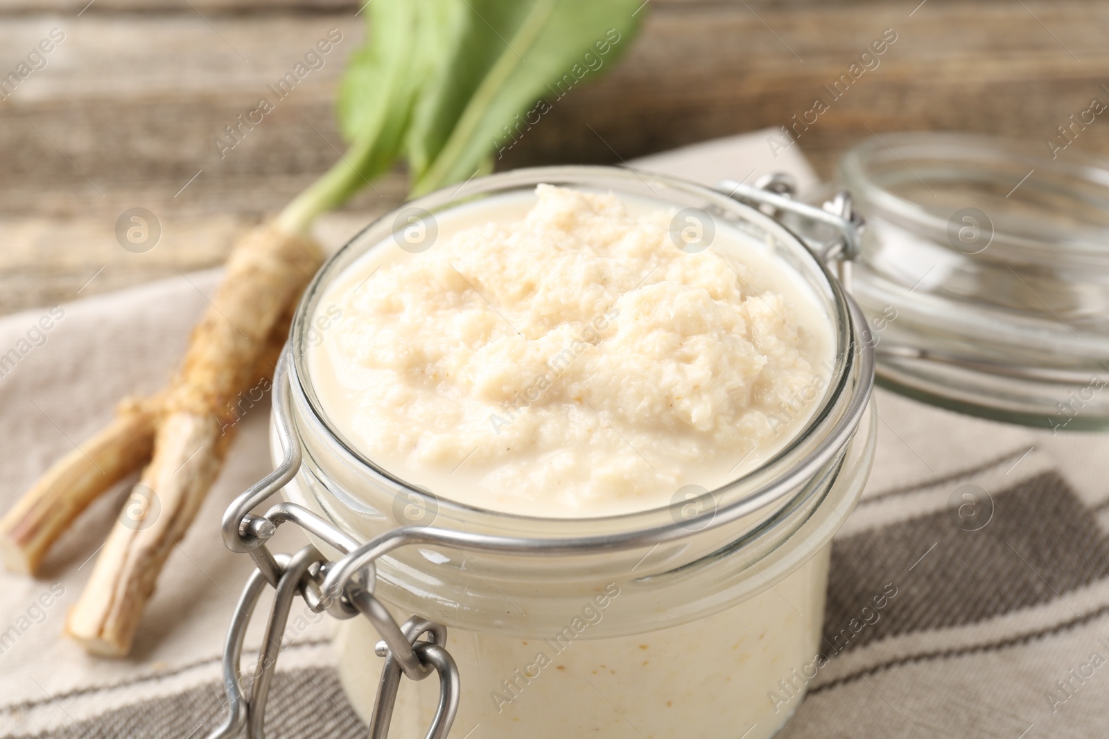 Photo of Tasty horseradish sauce and roots on wooden table, closeup