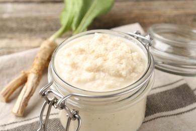 Photo of Tasty horseradish sauce and roots on wooden table, closeup
