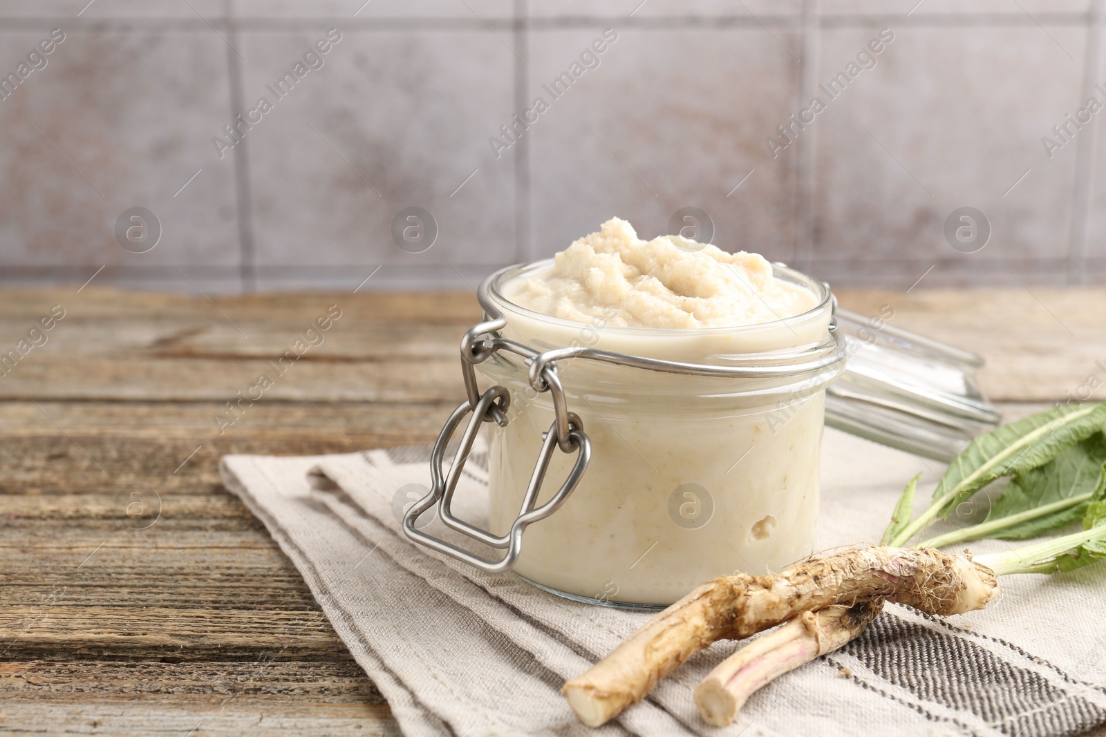 Photo of Tasty horseradish sauce and roots on wooden table, closeup. Space for text