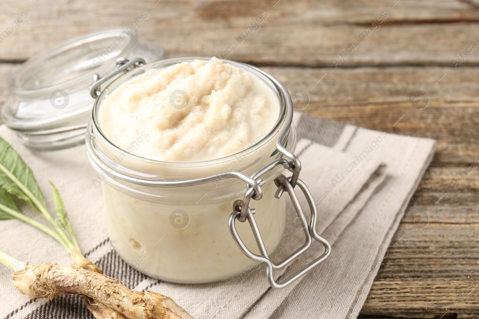 Photo of Tasty horseradish sauce and roots on wooden table, closeup
