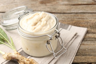 Photo of Tasty horseradish sauce and roots on wooden table, closeup