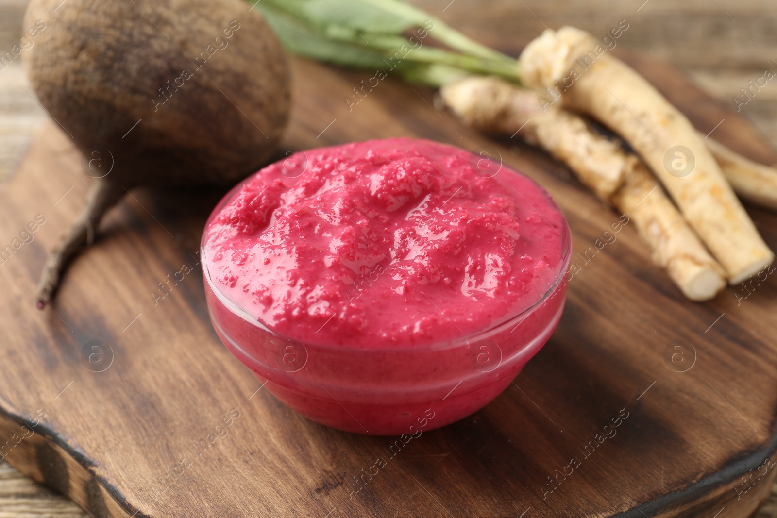 Photo of Tasty horseradish sauce with beetroot, roots and vegetable on wooden table, closeup