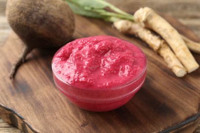 Photo of Tasty horseradish sauce with beetroot, roots and vegetable on wooden table, closeup