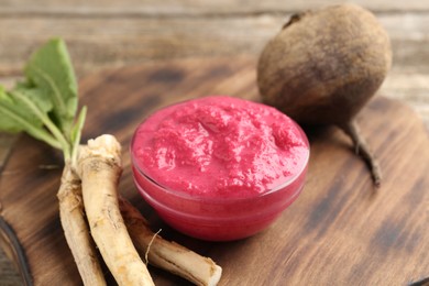 Photo of Tasty horseradish sauce with beetroot, roots and vegetable on wooden table, closeup