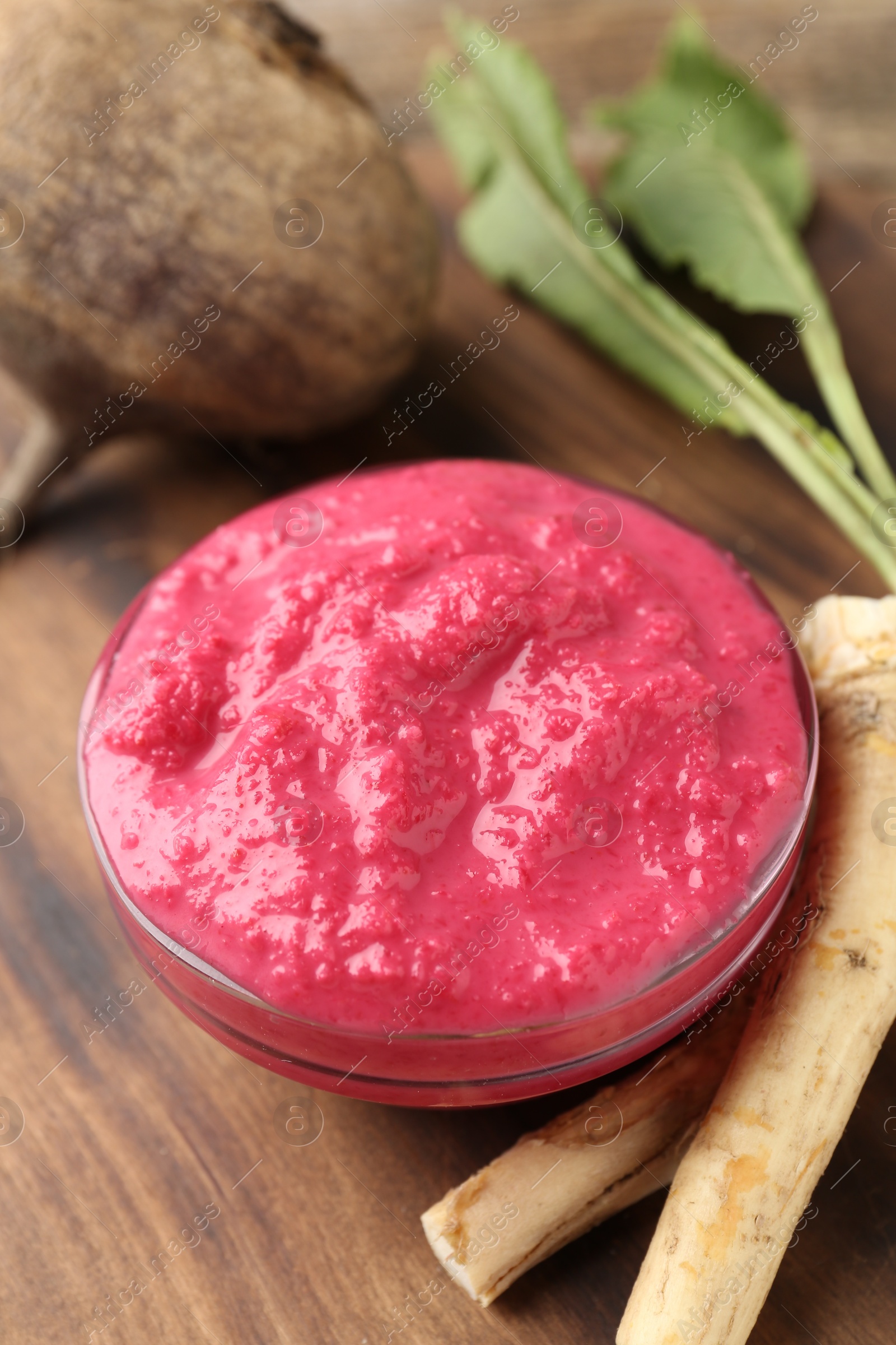 Photo of Tasty horseradish sauce with beetroot, roots and vegetable on wooden table, closeup