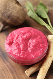 Photo of Tasty horseradish sauce with beetroot, roots and vegetable on wooden table, closeup