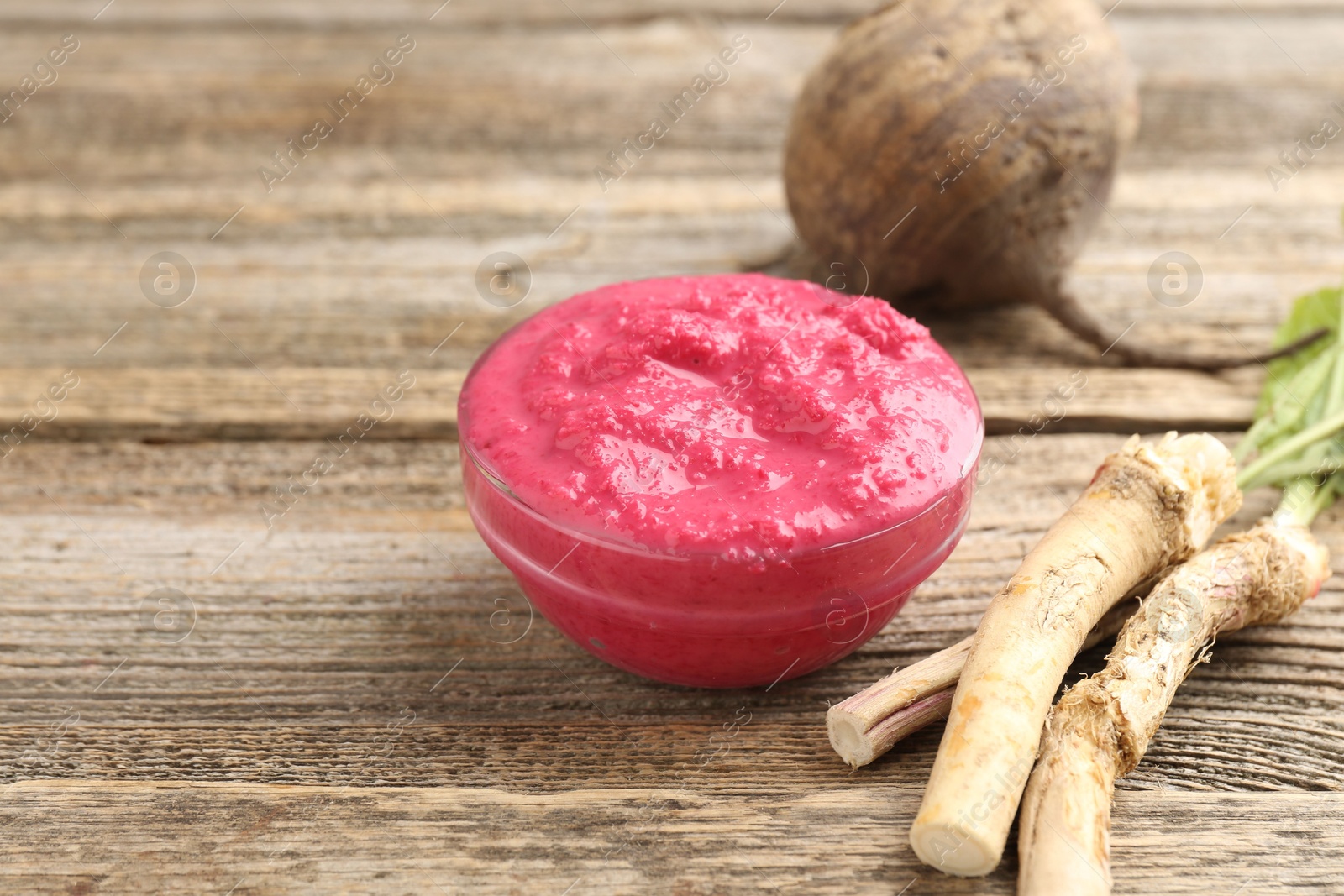 Photo of Tasty horseradish sauce with beetroot, roots and vegetable on wooden table, closeup. Space for text