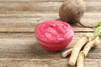 Photo of Tasty horseradish sauce with beetroot, roots and vegetable on wooden table, closeup. Space for text
