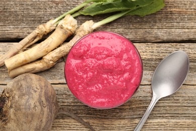 Photo of Tasty horseradish sauce with beetroot, spoon, roots and vegetable on wooden table, flat lay