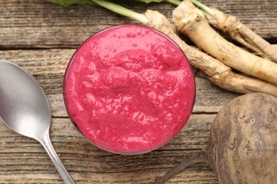 Photo of Tasty horseradish sauce with beetroot, spoon, roots and vegetable on wooden table, flat lay
