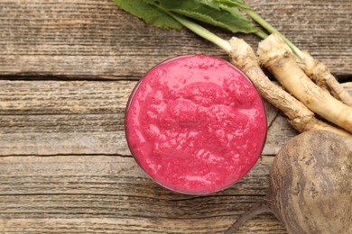 Photo of Tasty horseradish sauce with beetroot, roots and vegetable on wooden table, flat lay