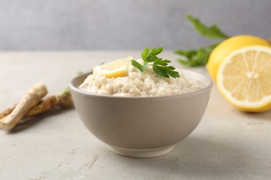 Photo of Tasty horseradish sauce with parsley, lemon slice and roots on light table, closeup
