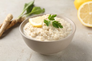 Photo of Tasty horseradish sauce with parsley, lemon slice and roots on light table, closeup