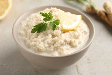 Photo of Tasty horseradish sauce with parsley and lemon slice on light table, closeup