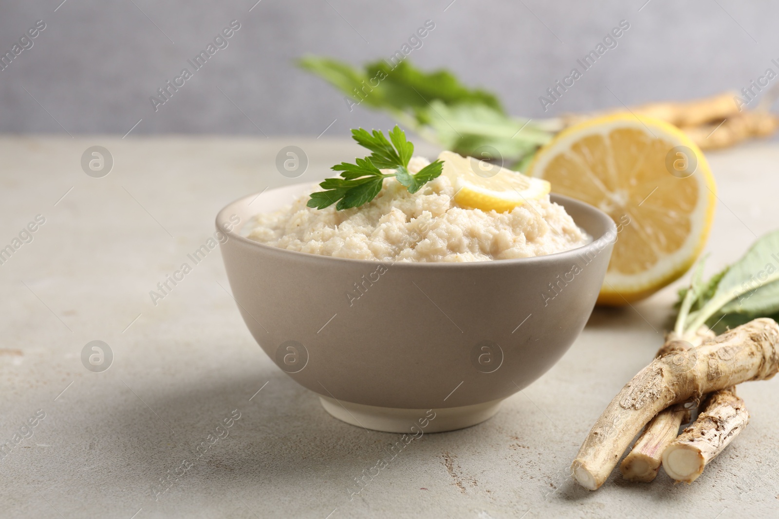 Photo of Tasty horseradish sauce with parsley, lemon slice and roots on light table, closeup