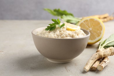 Photo of Tasty horseradish sauce with parsley, lemon slice and roots on light table, closeup