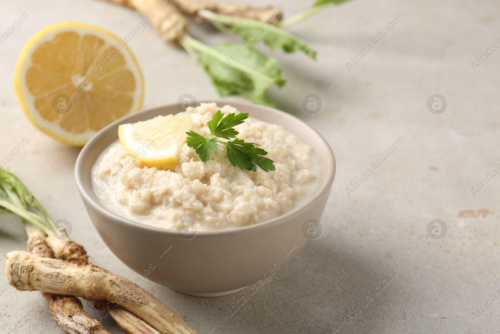 Photo of Tasty horseradish sauce with parsley, lemon slice and roots on light table, closeup. Space for text