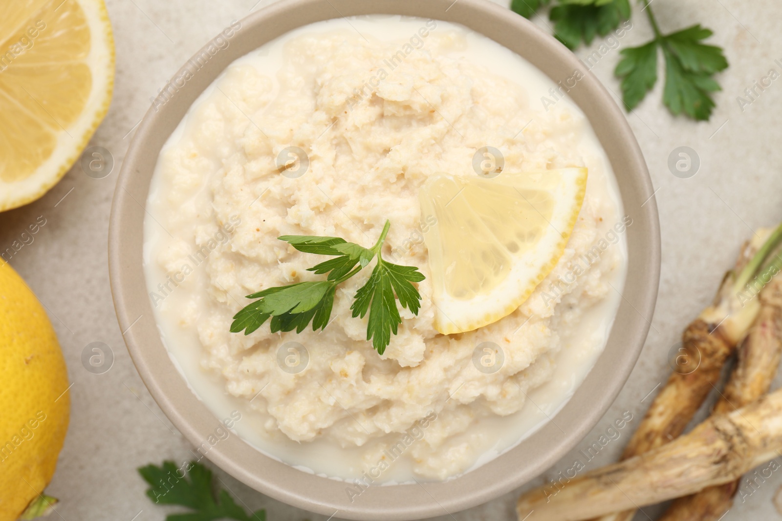 Photo of Tasty horseradish sauce with parsley, lemon slice and roots on light table, flat lay