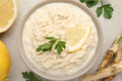 Photo of Tasty horseradish sauce with parsley, lemon slice and roots on light table, flat lay