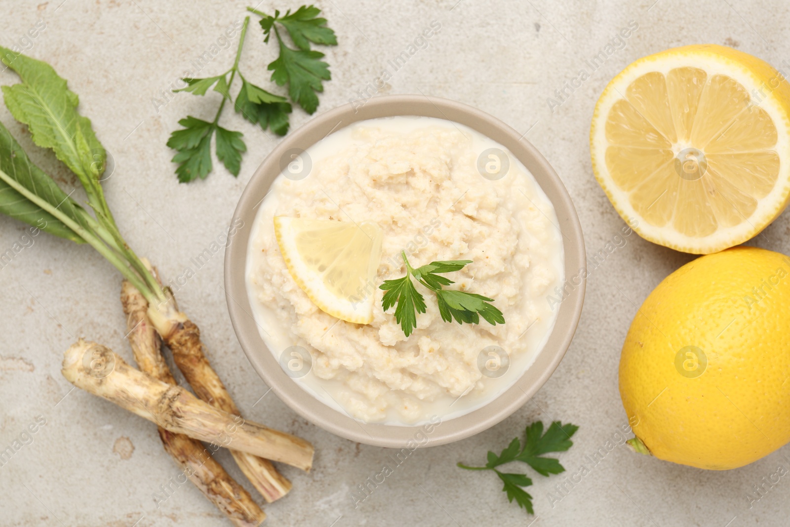 Photo of Tasty horseradish sauce with parsley, lemon slice and roots on light table, flat lay