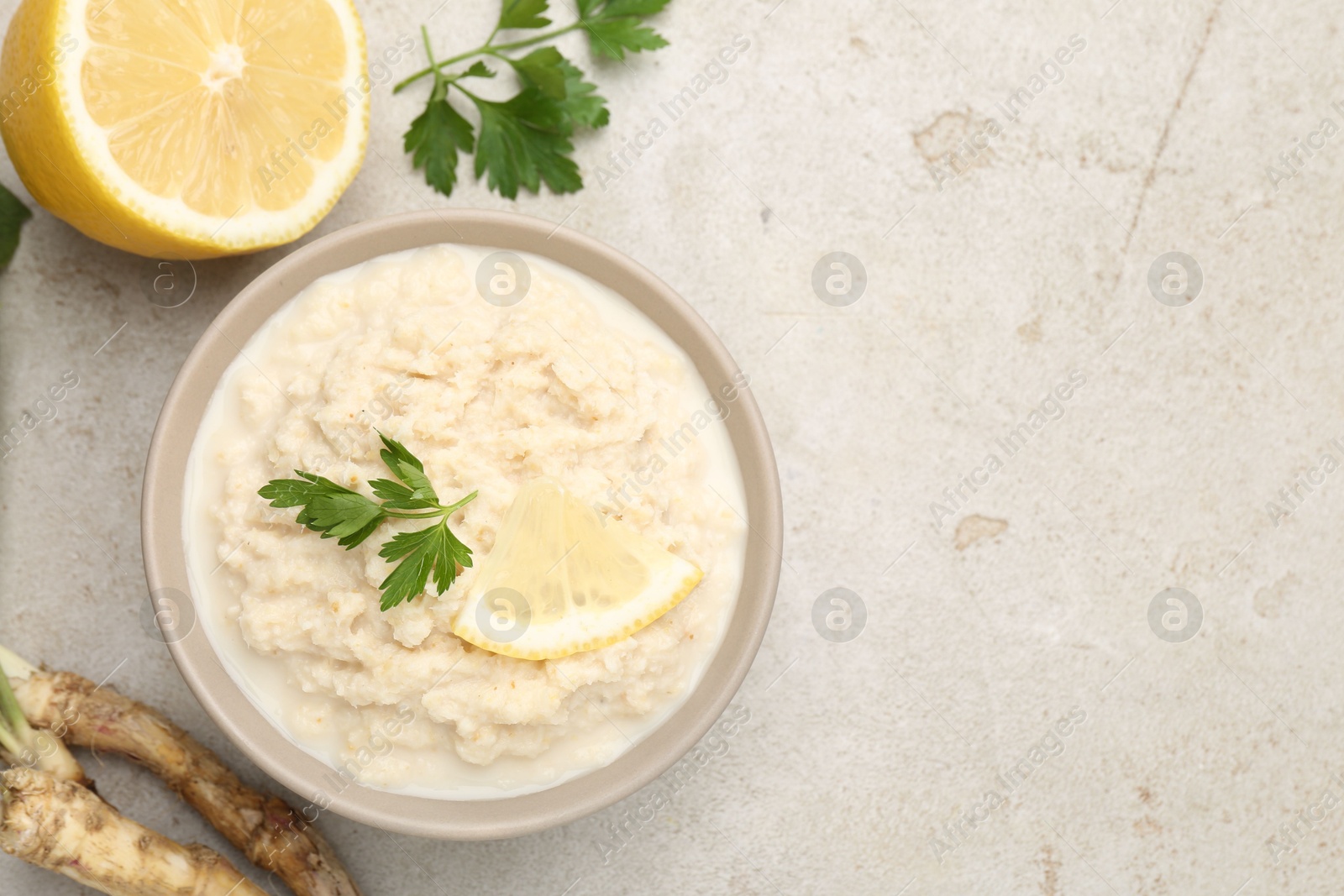 Photo of Tasty horseradish sauce with parsley, lemon slice and roots on light table, flat lay. Space for text