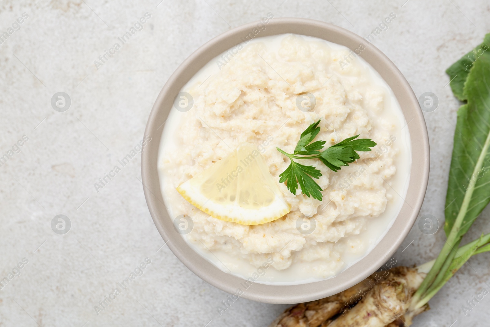 Photo of Tasty horseradish sauce with parsley, lemon slice and roots on light table, top view