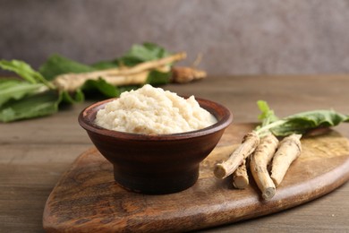 Photo of Tasty horseradish sauce and roots on wooden table, closeup