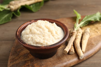 Photo of Tasty horseradish sauce and roots on wooden table, closeup