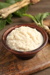 Photo of Tasty horseradish sauce and roots on wooden table, closeup