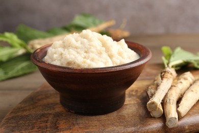 Photo of Tasty horseradish sauce and roots on wooden table, closeup